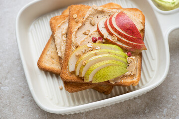Toasts with peanut butter and pear slices in a beige serving tray, middle closeup, horizontal shot, selective focus