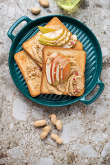 Green serving tray with peanut butter and pear toasts, above view on a brown granite background, vertical shot with space