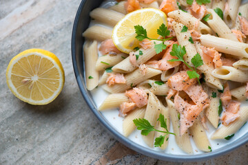 Creamy penne pasta with salmon flakes served in a grey plate, horizontal shot, middle close-up, selective focus