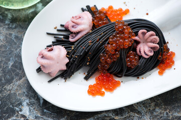 Squid-ink spaghetti with red caviar and baby octopuses on a white plate, close-up, horizontal shot