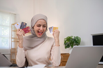 A young Muslim woman wearing a hijab is delighted to be able to order what she wants while shopping online happily while holding a credit card.