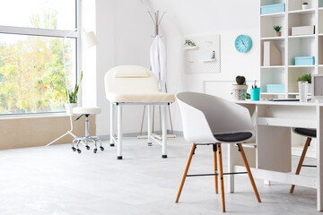 Interior of light medical office with workplace, couch and shelf unit