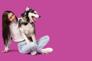 Beautiful young woman with Husky dog on purple background