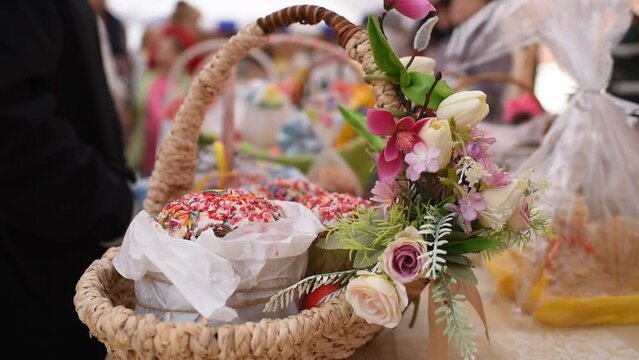 a basket with traditional pastries, Easter Kulich cake and colored eggs, in front of other baskets with Easter food. Many baskets are displayed on the table for the consecration and blessing of Easter