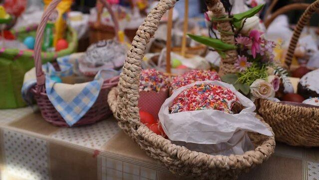 a basket with traditional pastries, Easter Kulich cake and colored eggs, in front of other baskets with Easter food. Many baskets are displayed on the table for the consecration and blessing of Easter