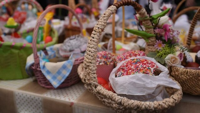 a basket with traditional pastries, Easter Kulich cake and colored eggs, in front of other baskets with Easter food. Many baskets are displayed on the table for the consecration and blessing of Easter