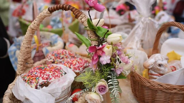 a basket with traditional pastries, Easter Kulich cake and colored eggs, in front of other baskets with Easter food. Many baskets are displayed on the table for the consecration and blessing of Easter
