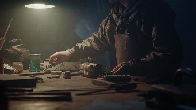 A man solders bomb elements in the dark workshop 
