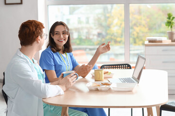 Young doctors with laptop having lunch at table in hospital kitchen