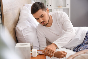 Young man taking pills before sleep in bedroom
