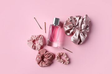 Bottle of perfume with scrunchies and hairpins on pink background
