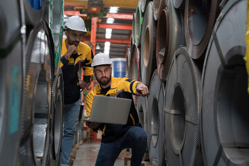 Two male engineers workers using laptop computer inspecting quality rolls of galvanized or metal...