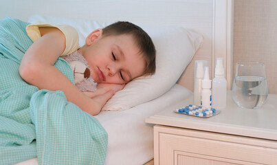 Fototapeta na wymiar Unhealthy sick boy hugging teddy bear sleeping in bed, resting at home in bedroom. Flu, ARVI, colds. Children's healthcare.