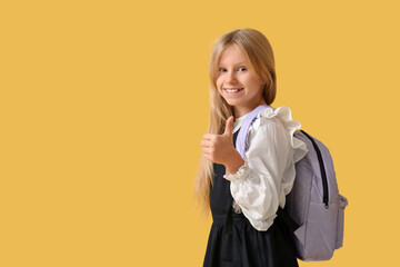 Cute schoolgirl with backpack on yellow background