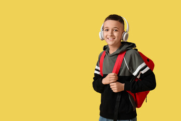 Cute schoolboy with headphones and backpack on yellow background