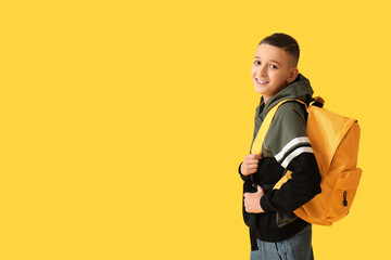 Cute schoolboy with backpack on yellow background