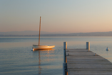 Voilier isolé amarré à côté d’un quai en bois au lever du soleil, sur les rives du lac...