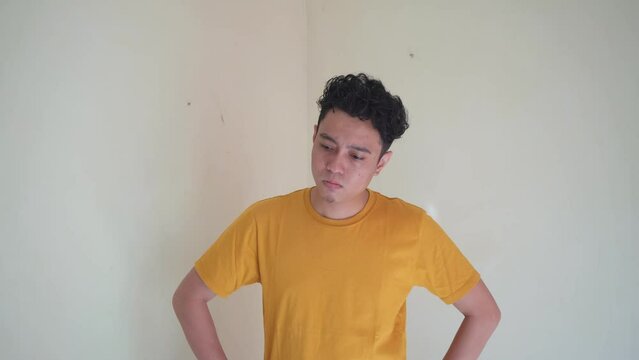 Young Indonesian curly man wear yellow t-shirt with overthinking expression. The footage is suitable to use for man expression and people advertising content media.