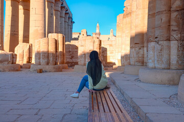 Luxor Temple at sunset, a large Ancient Egyptian temple complex located on the east bank of the Nile River - A young Egyptian girl is sitting on a bench and talking on the phone