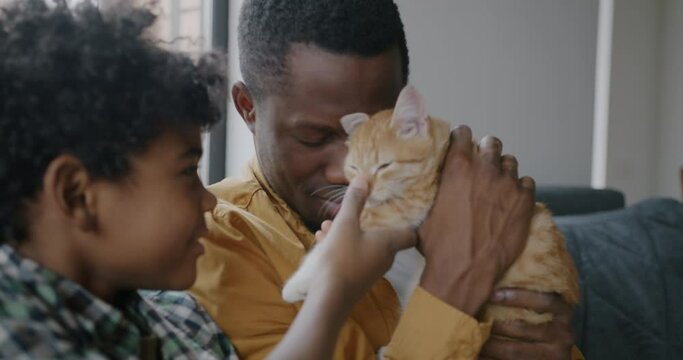 African American man and son little boy playing with domestic cat expressing love and care at home. Adorable kitten and people concept.