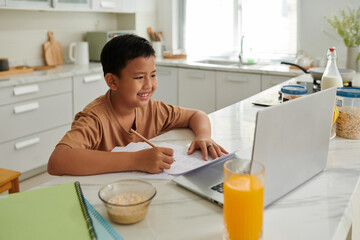 Smiling Vietnamese schoolboy watching video laptop when doing math homework