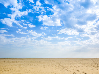Fototapeta na wymiar The background texture of a vast expanse of beach sands, with visitors' footprints, and clouds scattered in a pattern on sky. Concept of a peaceful, breezy day at the seaside. Copy space for design.