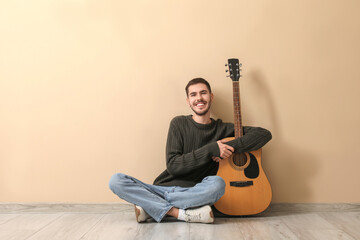 Handsome young man with guitar on beige background