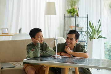 Dreamy father and son looking at small model of wind turbine with rotating blades