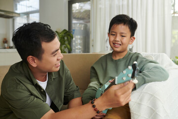 Smiling father teaching son playing ukulele