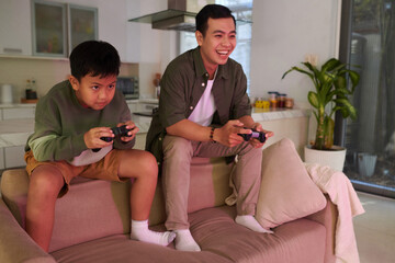 Determined preteen Vietnamese boy playing videogames with father