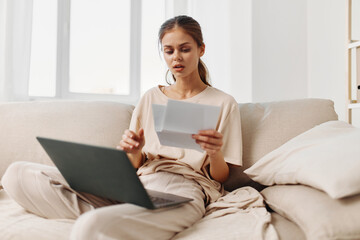 Smiling woman using laptop in cozy living room, a perfect blend of comfort and productivity.