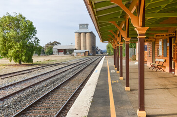 Fototapeta na wymiar The historic Coolamon Railway Station platform overlooks train tracks with silos stand tall in the background. Concept of rural transportation and agriculture in the Australian countryside.
