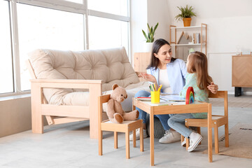 Female psychologist with little girl reading book at table in office