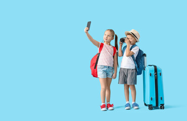 Cute little children with backpacks, suitcase and camera taking selfie on blue background. Travel concept