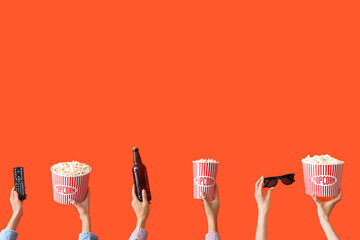 Many hands with buckets of popcorn, beer and TV remote on orange background