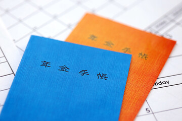 Japanese pension insurance booklets on table with calendar. Blue and orange pension book for japan...