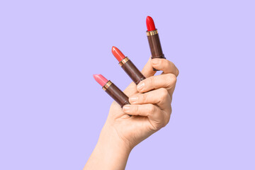Female hand with different lipsticks on lilac background