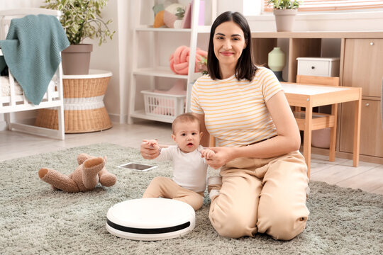 Happy mother with her little baby and robot vacuum cleaner on carpet in bedroom