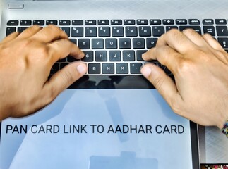 Picture of a person working on laptop. Placard with PAN CARD LINK TO AADHAR CARD written on it.