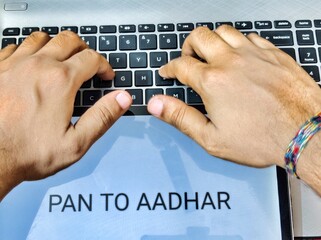 Picture of a person working on laptop. Placard with PAN TO AADHAR written on it.