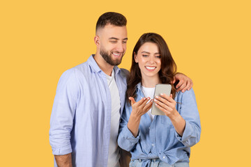 Couple using phone together on yellow background