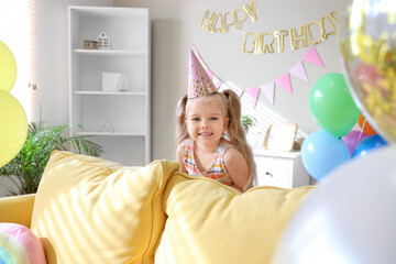 Cute little girl in party hat with balloons and decorations for birthday at home