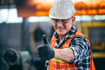 Portrait of male foreman factory wearing hardhat showing thumbs up looking at camera standing at the industry factory. Construction worker or builder career in positive attitude. copy space