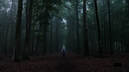 Static shot of a man from his back wearing hoody and running along the forest with long trees
