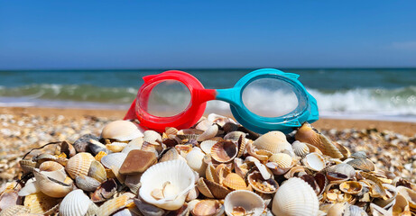 There are swimming goggles on the shells against the background of blue sea waves. Banner with the...