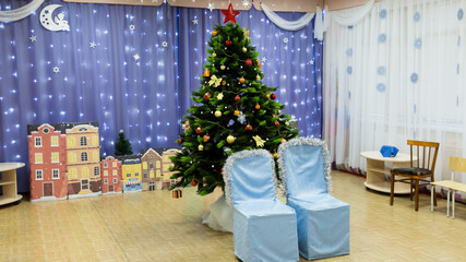 Empty decorated hall kindergarten with a New Year tree before a concert.