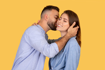 Man kissing woman on cheek against yellow