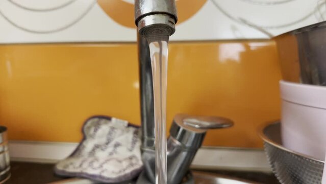 Chlorinated water flows from a stainless steel faucet with orange tiles in the kitchen