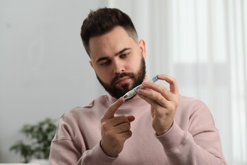 Diabetes test. Man checking blood sugar level with lancet pen at home, selective focus