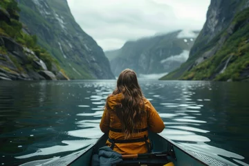Fotobehang A woman in a yellow jacket is sitting in a canoe on a lake. The water is calm and the sky is cloudy. The woman is enjoying the peacefulness of the scene © vefimov